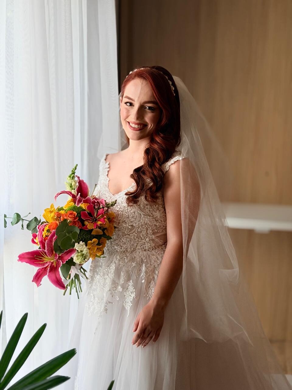 Noiva ruiva sorrindo com buquê tropical e véu longo